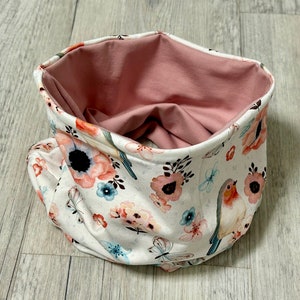 Könnte beinhalten: Ein Schlauchschal mit floralem Muster und weichem rosa Innenfutter. Das Design zeigt Blumen, Schmetterlinge und Vögel. Dieser vielseitige Schal ist ein modisches Accessoire.