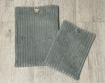 Peut inclure: Deux articles en tissu de velours côtelé gris, un plus grand et un plus petit, sont présentés. Chacun a un bouton attaché en haut. Le velours côtelé a des rayures verticales. Les articles sont probablement des sets de table ou similaires.