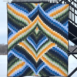 May include: A rectangular quilt featuring a geometric pattern of small squares in shades of orange, light blue, dark blue, and forest green. The design creates a symmetrical, diamond-like motif with a black border, hanging from a metal rod.