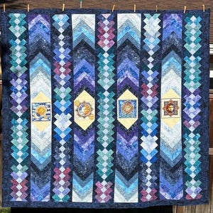 Peut inclure: Une grande courtepointe faite à la main sur le thème céleste. La courtepointe présente un fond bleu foncé avec des colonnes verticales de différentes nuances de bleu, de violet et de sarcelle. Quatre panneaux jaunes avec des motifs de soleil et de lune sont espacés.