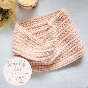 Op de afbeelding: Een lichtroze gehaakte col met een gestructureerd patroon van horizontale ribbels en stervormige steken. Een rond wit label is over de afbeelding geplaatst met de tekst Starry Ridge Cowl Crochet Pattern 3 Sizes en een PDF-pictogram.
