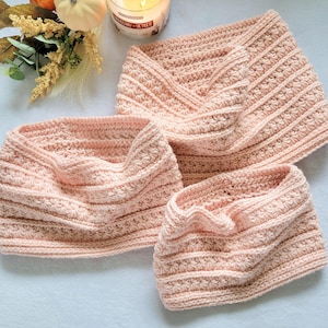May include: Three light pink crochet cowls featuring a textured star stitch pattern arranged in horizontal rows. Each cowl is crafted from soft yarn and displays a consistent knit-like appearance with a folded edge design for a layered look.