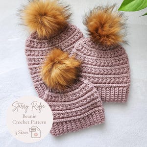 May include: Two mauve crochet beanies with textured horizontal ridges and large, fluffy, golden-brown faux fur pom-poms on top. A circular label displays the text Starry Ridge Beanie Crochet Pattern 3 Sizes with a PDF file icon.