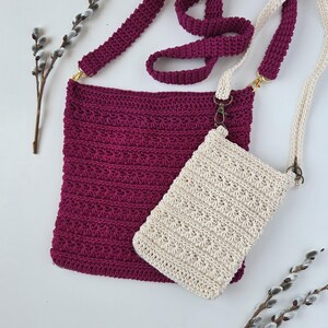 May include: Two handmade crochet bags. One is a deep magenta colour, the other is a cream colour. Both have long straps and a textured stitch pattern. The larger bag has gold-coloured hardware, while the smaller bag has bronze-coloured hardware.