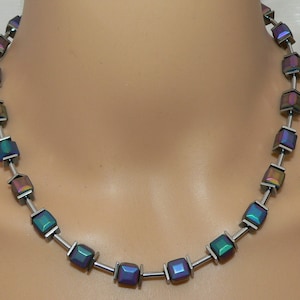 May include: A silver necklace with iridescent square beads. The beads have a blue, green, and purple color.