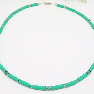 Puede incluir: Un collar verde y plateado con pequeñas cuentas redondas y cuentas cilíndricas más grandes.