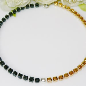 May include: A black and gold necklace made of square beads. The necklace is made of two halves, one black and one gold.
