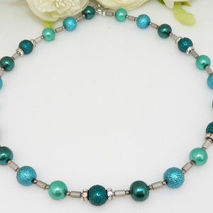 May include: A teal and green beaded necklace with silver accents. The beads are round and have a textured surface.