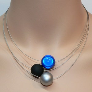 May include: A silver chain necklace with three round beads. The beads are black, silver, and blue.