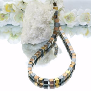 May include: A necklace made of square-shaped hematite beads in shades of gold, silver, and black.