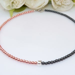 May include: A necklace with half rose gold beads and half black hematite beads separated by a silver bead.
