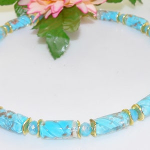May include: A turquoise beaded necklace with gold-colored accents. The necklace features cylindrical beads with a textured design, interspersed with gold-toned spacers. The beads have a marbled appearance with brown and turquoise hues.