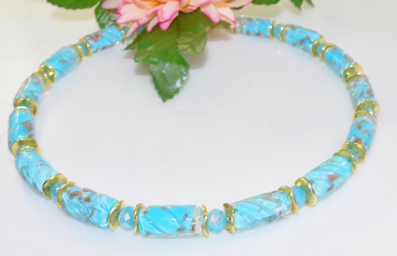 May include: A turquoise beaded necklace with gold-colored accents. The necklace features cylindrical beads with a textured design, interspersed with gold-toned spacers. The beads have a marbled appearance with brown and turquoise hues.