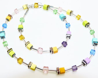 May include: A colorful necklace with square beads in shades of yellow, green, blue, purple, and pink. The beads are separated by silver metal bars.