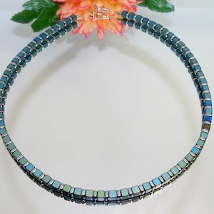 May include: A double-strand necklace made of small, square, iridescent blue and green beads. The necklace is made of metal and has a silver finish.