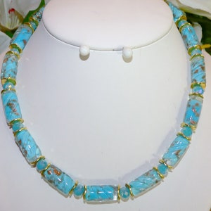 May include: A turquoise beaded necklace with gold accents. The necklace features cylindrical beads with a swirled pattern and gold-colored spacers. The necklace is displayed on a white bust, showcasing the jewelry's design and color.