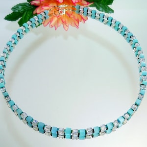 May include: A double-strand necklace made of turquoise and clear square beads. The necklace is on a white background.