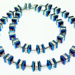 May include: A blue and silver necklace with square-shaped beads. The beads are set with clear crystals and have a metallic finish.