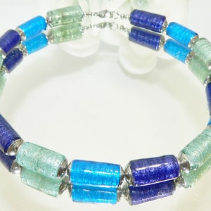 May include: A double-strand necklace with blue, teal, and green glass beads. The beads are cylindrical and have a sparkly finish. The necklace is made with silver-toned metal connectors.