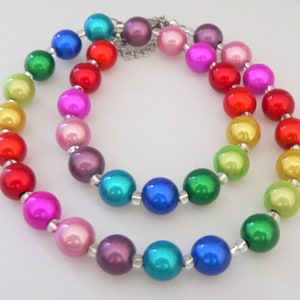 Peut inclure: Un collier de perles multicolores arc-en-ciel avec un fermoir argenté. Les perles sont irisées et ont une finition nacrée.
