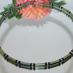 May include: A double-strand necklace made of iridescent green and black beads. The beads are cylindrical and have a metallic sheen. The necklace is fastened with a silver clasp.