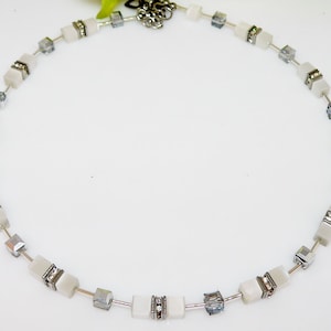May include: A white necklace with square-shaped beads and silver accents. The beads are interspersed with clear crystal beads.