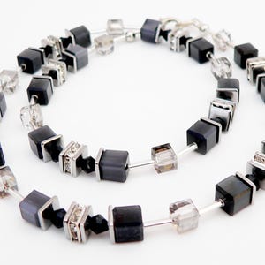 May include: A necklace featuring a repeating pattern of black square beads, clear cube beads, and silver-toned square accents. The necklace is strung on a thin, silver-colored wire and is displayed against a white background.