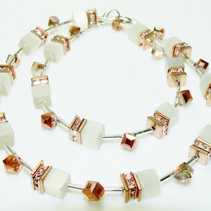 May include: A white and rose gold necklace with square-shaped beads and crystal accents.