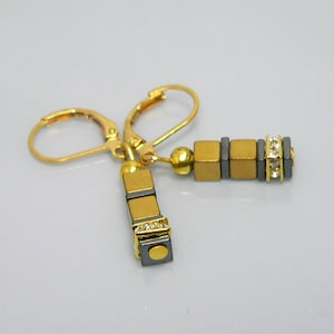 May include: Gold and black dangle earrings with a cubic zirconia accent. The earrings have a leverback closure.