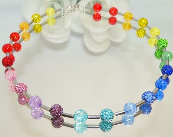 May include: A double-strand necklace with rainbow colored beads. The beads are round and have a sparkly finish. The necklace is made of silver metal.
