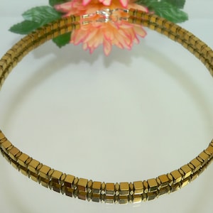 May include: A gold-toned necklace made of square-shaped beads. The necklace is double-stranded and has a simple design.