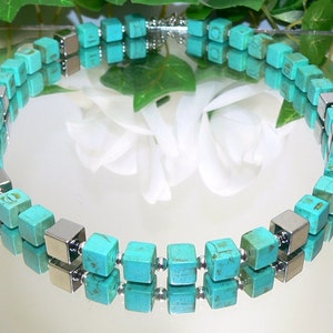 May include: A turquoise and silver necklace with square beads. The necklace is made of two strands of turquoise beads, with silver beads interspersed between them.