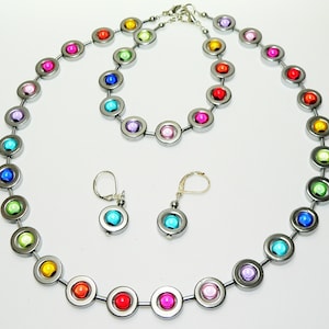 May include: A jewelry set featuring a necklace, bracelet, and earrings. The set includes a necklace and bracelet with a series of silver-toned circular links, each containing a colorful, round bead. The earrings have a similar design.
