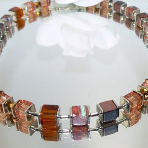 Può includere: Una collana d'argento con perline quadrate di vetro marrone e trasparente. Le perline sono disposte in un motivo ripetitivo.