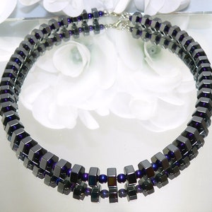 May include: A double-strand necklace made of dark gray and purple square-shaped beads.