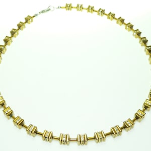 May include: A gold necklace with a geometric design. Each link is a small square with a pointed top and bottom, and is accented with clear rhinestones.