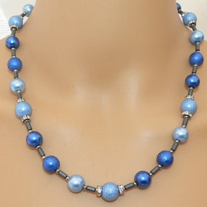 May include: A blue and light blue beaded necklace with silver accents. The beads are round and have a sparkly finish.