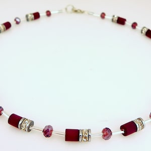 May include: A silver necklace with burgundy velvet beads and clear crystal accents.