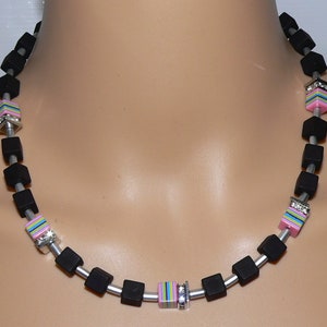 May include: A black and silver necklace with pink, blue, and green striped beads. The beads are square shaped and have rhinestones.