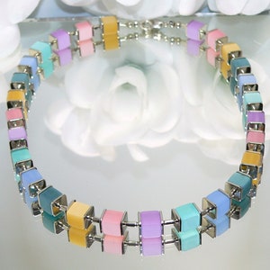 May include: A pastel coloured necklace with square beads in shades of blue, green, yellow, pink, and purple. The necklace is made of metal and has a silver finish.