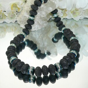May include: A black lava rock beaded necklace with silver and blue accents. The beads are round and have a rough texture. The necklace is layered and has a double strand of beads.