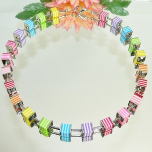 May include: A rainbow colored necklace made of square beads with white stripes. The necklace is made of metal and has a silver finish.