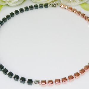 May include: A black and rose gold necklace with square beads. The necklace is made of two different colors of beads, with the black beads on one side and the rose gold beads on the other.