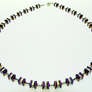 May include: A silver necklace with a chain of alternating square-shaped beads. The beads are a deep purple with iridescent accents and are set with clear crystals.