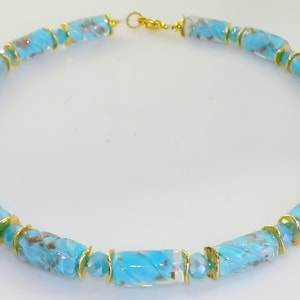 May include: A turquoise and gold beaded necklace. The necklace features cylindrical beads with a marbled effect, interspersed with gold-colored spacers. The necklace is approximately 18 inches in length and has a gold-colored clasp.