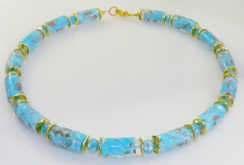 May include: A turquoise and gold beaded necklace. The necklace features cylindrical beads with a marbled effect, interspersed with gold-colored spacers. The necklace is approximately 18 inches in length and has a gold-colored clasp.