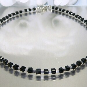 May include: A silver chain necklace with black square-shaped beads.