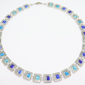 May include: A silver necklace with square-shaped blue glass beads. The beads are graduated in size and color, with the largest and darkest blue beads in the center of the necklace.