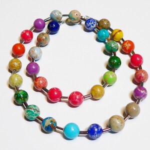 Könnte beinhalten: Eine bunte Perlenkette mit einem Regenbogen an Farben, darunter Rot, Orange, Gelb, Grün, Blau und Lila. Die Perlen sind durch silberne Metallabstandshalter getrennt.