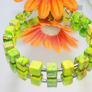 Könnte beinhalten: Ein grünes und gelbes Edelstein-Armband mit quadratischen Perlen. Das Armband besteht aus zwei Perlenreihen mit silbernen Abstandshaltern zwischen den Perlen.
